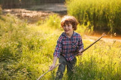 Photo of Cute little boy playing with wooden sticks in nature