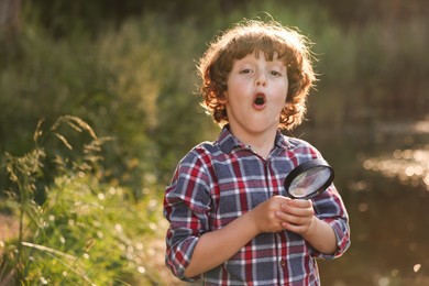 Photo of Cute little boy with magnifying glass in nature