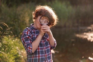 Photo of Cute little boy looking through magnifying glass in nature