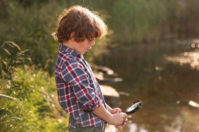 Photo of Cute little boy looking through magnifying glass in nature