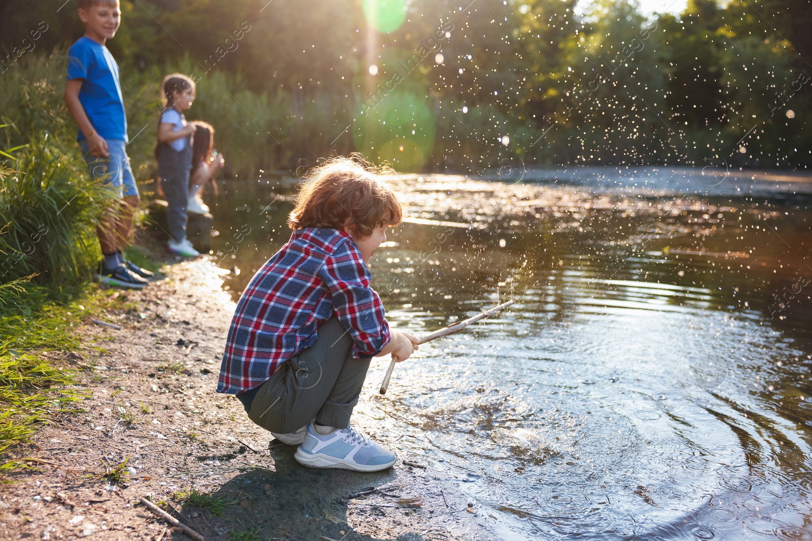 Cute little boy and other children playing by lake in nature, selective focus Photo of Cute little boy and other children playing by lake in nature, selective focus