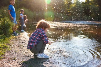 Photo of Cute little boy and other children playing by lake in nature, selective focus