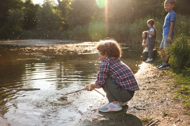 Photo of Cute little boy and other children playing by lake in nature, selective focus