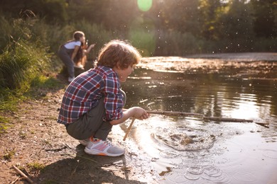 Photo of Cute little boy and other children playing by lake in nature, selective focus