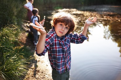 Photo of Cute little boy and other children playing by lake in nature, selective focus