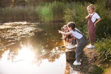 Photo of Children playing with magnifying glass by lake in nature