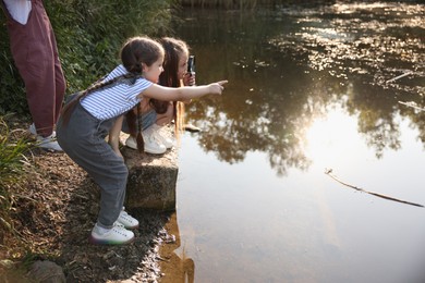 Photo of Children playing with magnifying glass by lake in nature