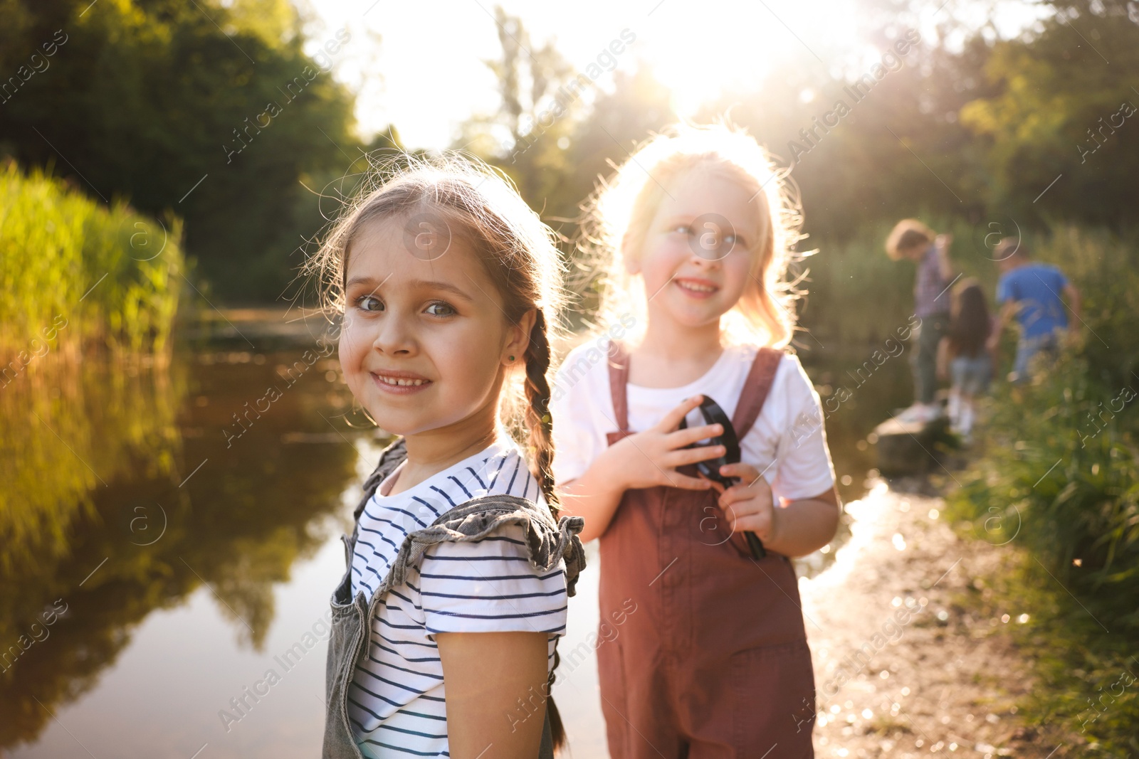 Children spending time in nature. Cute little girls by lake, selective focus Photo of Children spending time in nature. Cute little girls by lake, selective focus