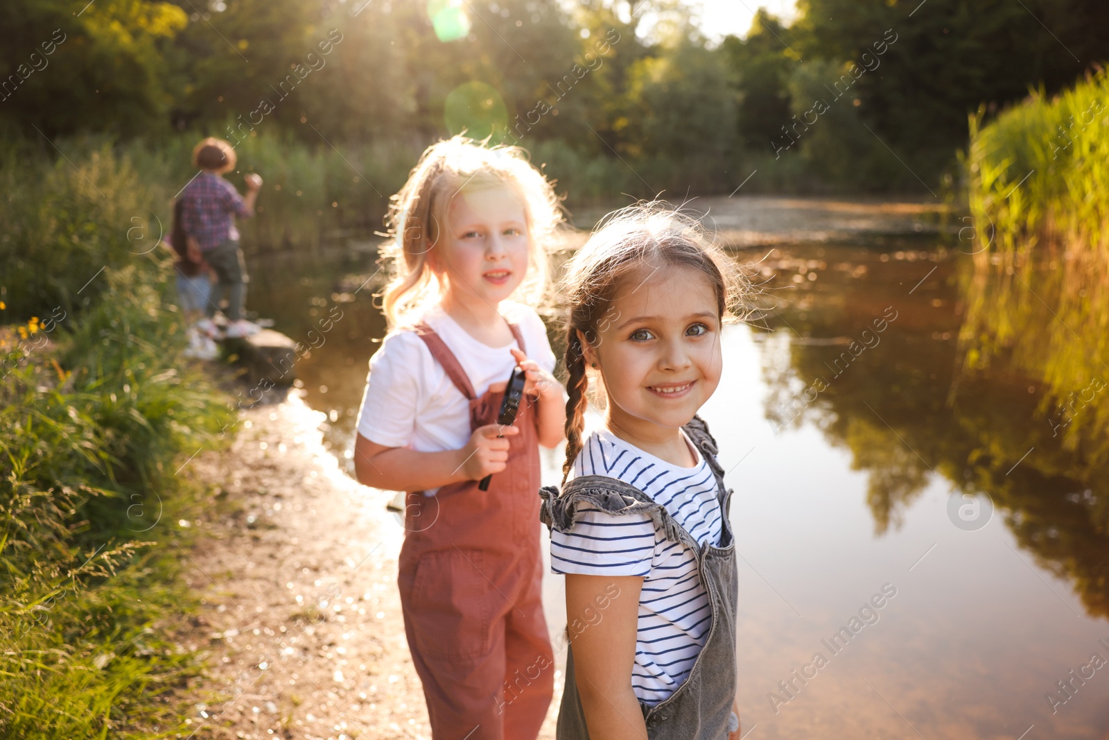 Children spending time in nature. Cute little girls by lake, selective focus Photo of Children spending time in nature. Cute little girls by lake, selective focus