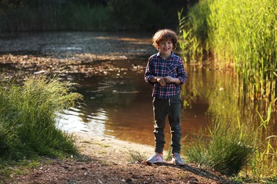 Photo of Cute little boy standing by lake in nature