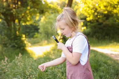 Photo of Cute little girl looking at plant through magnifying glass in nature