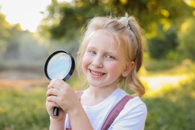 Photo of Cute little girl with magnifying glass in nature, closeup