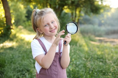 Photo of Cute little girl with magnifying glass in nature