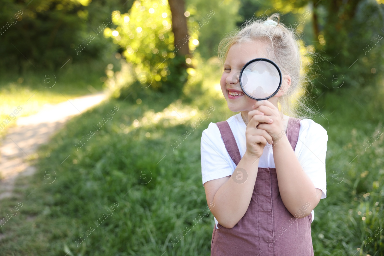 Cute little girl looking through magnifying glass in nature. Space for text Photo of Cute little girl looking through magnifying glass in nature. Space for text