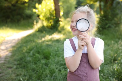 Photo of Cute little girl looking through magnifying glass in nature. Space for text