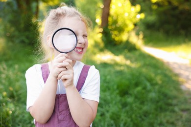 Photo of Cute little girl looking through magnifying glass in nature. Space for text