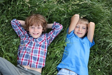Photo of Cute little boys lying on grass in nature, top view