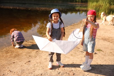 Photo of Children with paper boat and fish spending time by lake in nature