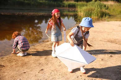 Photo of Children with paper boat and fish spending time by lake in nature