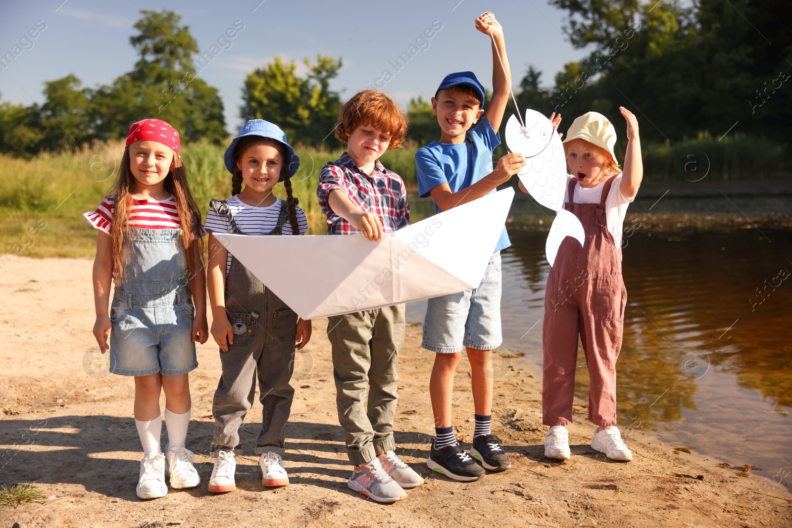 Children with paper boat and fish by lake in nature Photo of Children with paper boat and fish by lake in nature