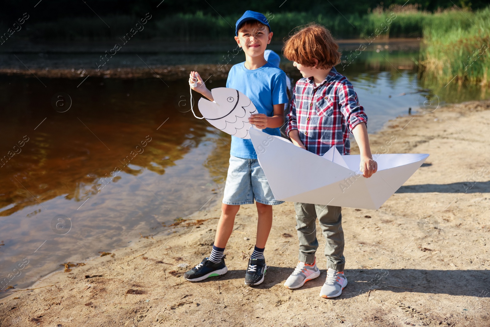 Cute little boys with paper boat and fish by lake in nature Photo of Cute little boys with paper boat and fish by lake in nature
