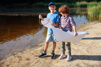Photo of Cute little boys with paper boat and fish by lake in nature