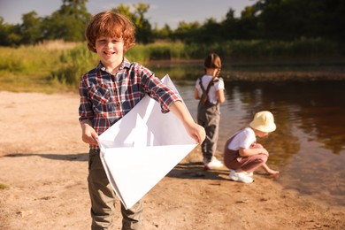 Photo of Children in nature, selective focus. Cute little boy with paper boat by lake