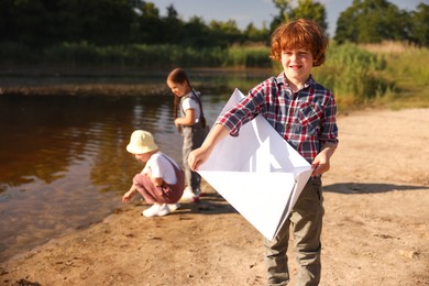 Photo of Children in nature, selective focus. Cute little boy with paper boat by lake