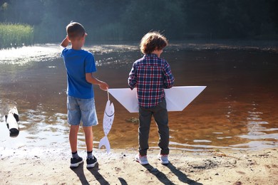 Photo of Children with paper boat and fish by lake in nature