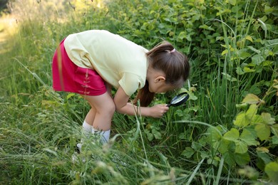 Photo of Cute little girl looking at plant through magnifying glass in nature