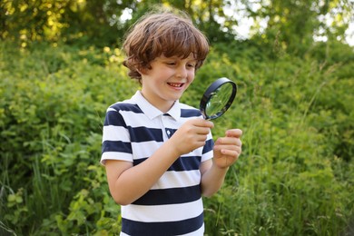 Photo of Cute little boy looking at plant through magnifying glass in nature