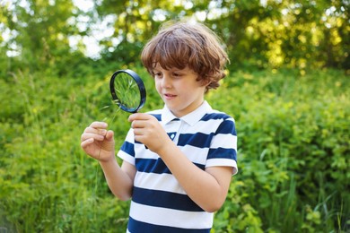 Photo of Cute little boy looking at plant through magnifying glass in nature