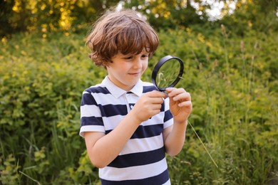 Photo of Cute little boy looking at plant through magnifying glass in nature