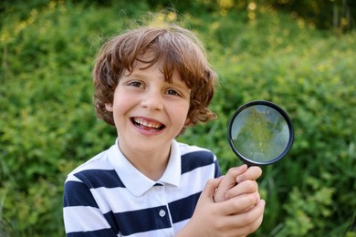 Photo of Cute little boy with magnifying glass in nature