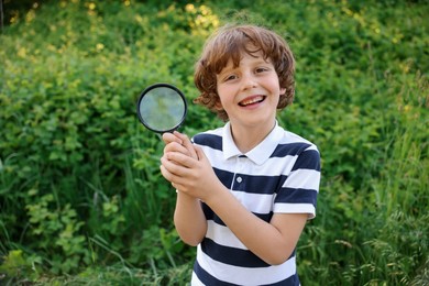 Photo of Cute little boy with magnifying glass in nature