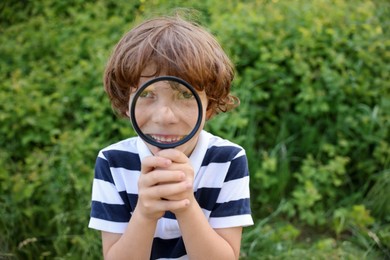 Photo of Cute little boy looking through magnifying glass in nature