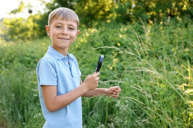 Photo of Cute little boy with magnifying glass in nature. Space for text