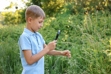 Photo of Cute little boy looking at plants through magnifying glass in nature
