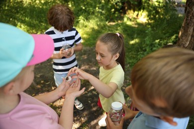 Photo of Children in nature. Cute little girl putting snail into jar outdoors