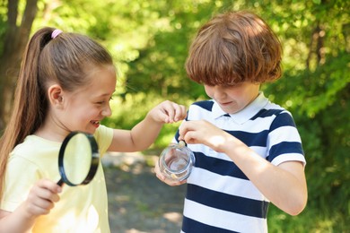 Photo of Children looking at jar with snail through magnifying glass in nature