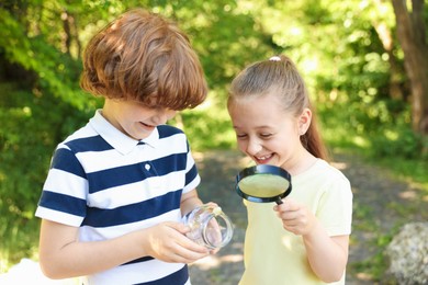 Photo of Children looking at jar with snail through magnifying glass in nature