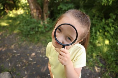 Photo of Cute little girl looking through magnifying glass in nature