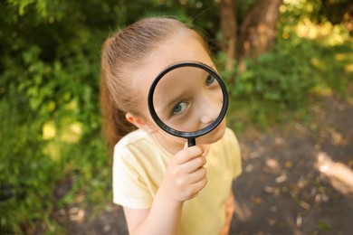 Photo of Cute little girl looking through magnifying glass in nature