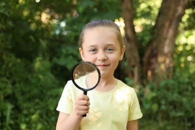 Photo of Cute little girl with magnifying glass in nature