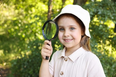 Photo of Cute little girl with magnifying glass in nature