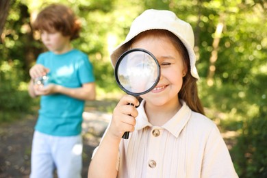 Photo of Cute little girl looking through magnifying glass in nature, selective focus