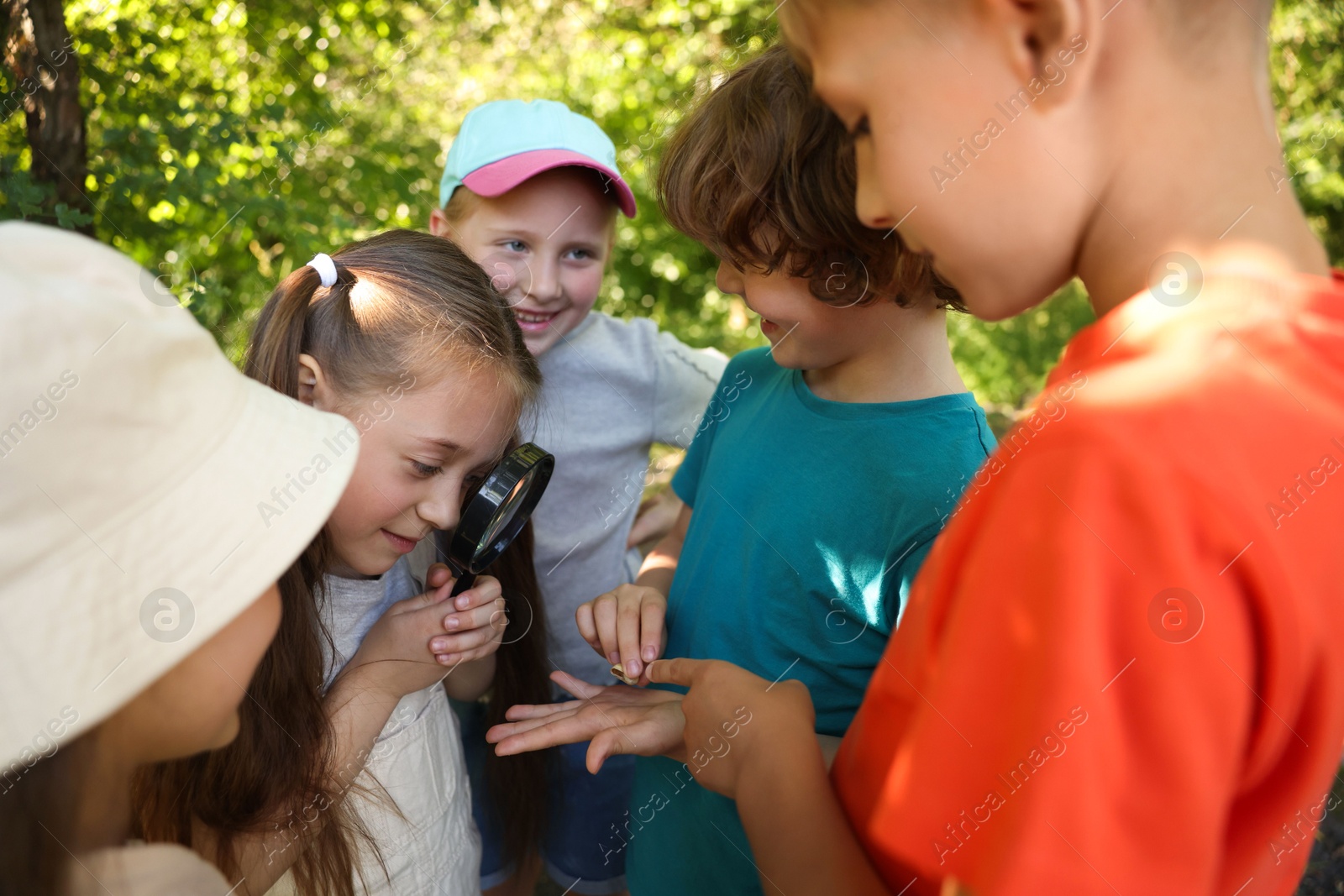Photo of Children looking at snail through magnifying glass in nature