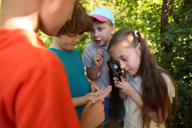 Photo of Children looking at snail through magnifying glass in nature