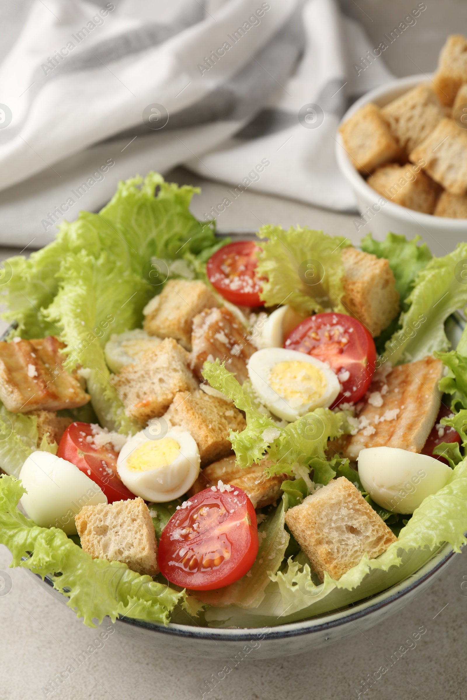 Photo of Delicious salad with croutons, chicken, quail eggs, tomato and cheese on grey table, closeup