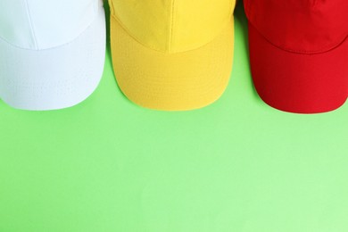 Photo of Colorful baseball hats on light green background, top view. Space for text